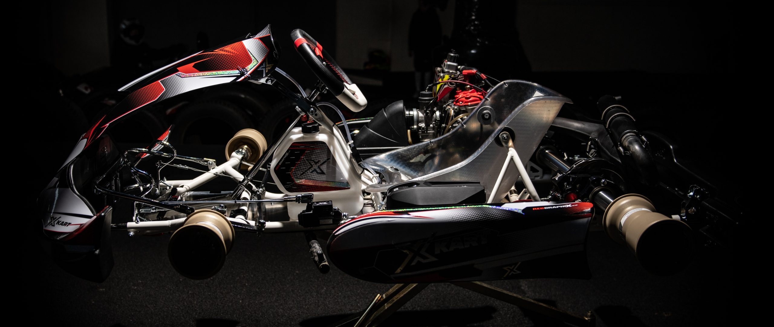image of XKART chassis or TB KART from italy, white chassis with striking red and black livery of xkart team side view with magnesium kart wheels